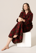 Woman wearing a red and black plaid nightshirt sitting on a white stool against a beige background