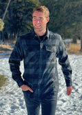 A man wearing a long-sleeved black and grey buffalo check flannel shirt with two breast pockets and a button cuff.