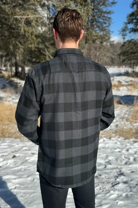 Back view of man wearing a long-sleeved black and grey buffalo check flannel shirt with two breast pockets and a button cuff.