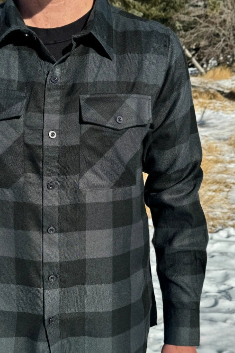 Close up of man wearing a long-sleeved black and grey buffalo check flannel shirt with two breast pockets and a button cuff.