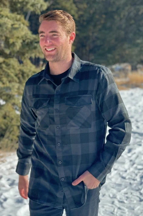 A man wearing a long-sleeved black and grey buffalo check flannel shirt with two breast pockets and a button cuff.