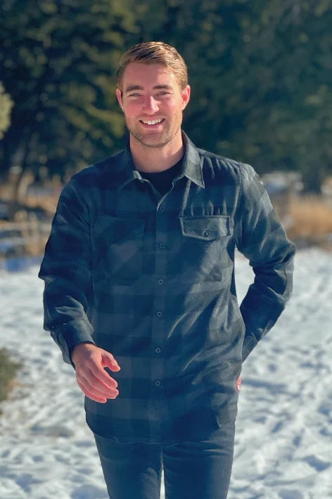 A man wearing a long-sleeved black and grey buffalo check flannel shirt with two breast pockets and a button cuff.