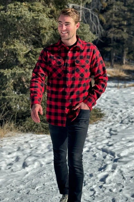A man wearing a red and black buffalo check flannel shirt with two flap breast pockets and a button cuff, standing outdoors.