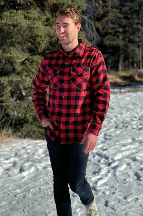 A man wearing a red and black buffalo check flannel shirt with two flap breast pockets and a button cuff, standing outdoors.