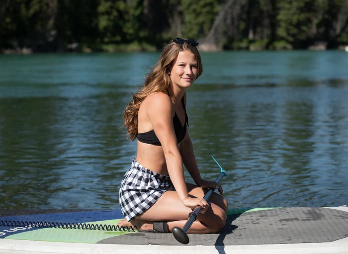A girl paddle boarding wearing black and white buffalo check shorts