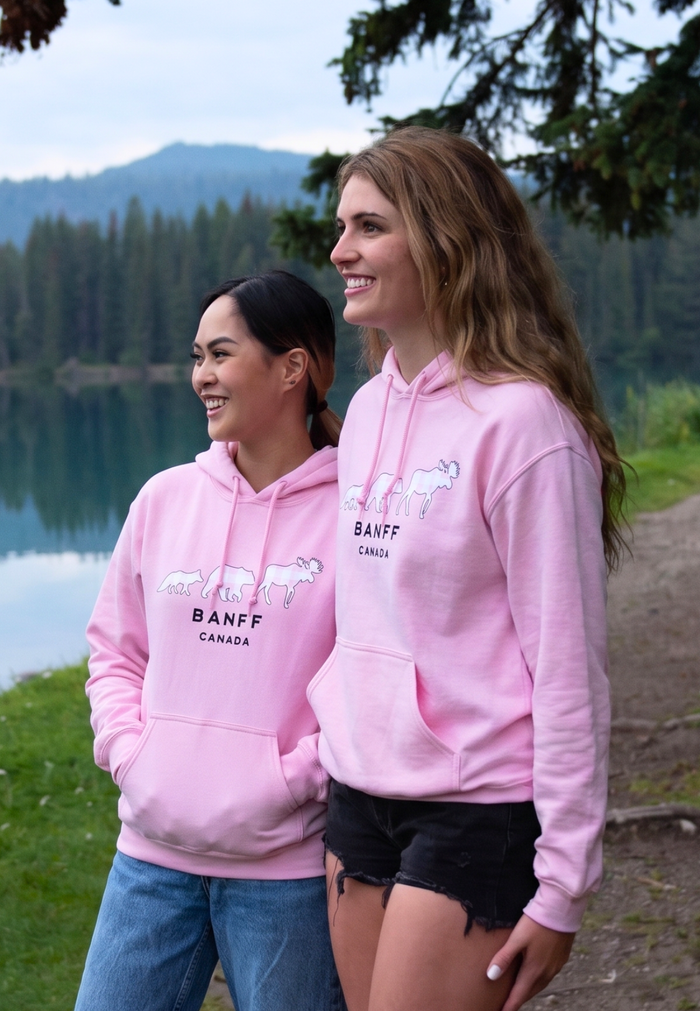 Two women wearing pink hoodies with Banff branding by a lake.
