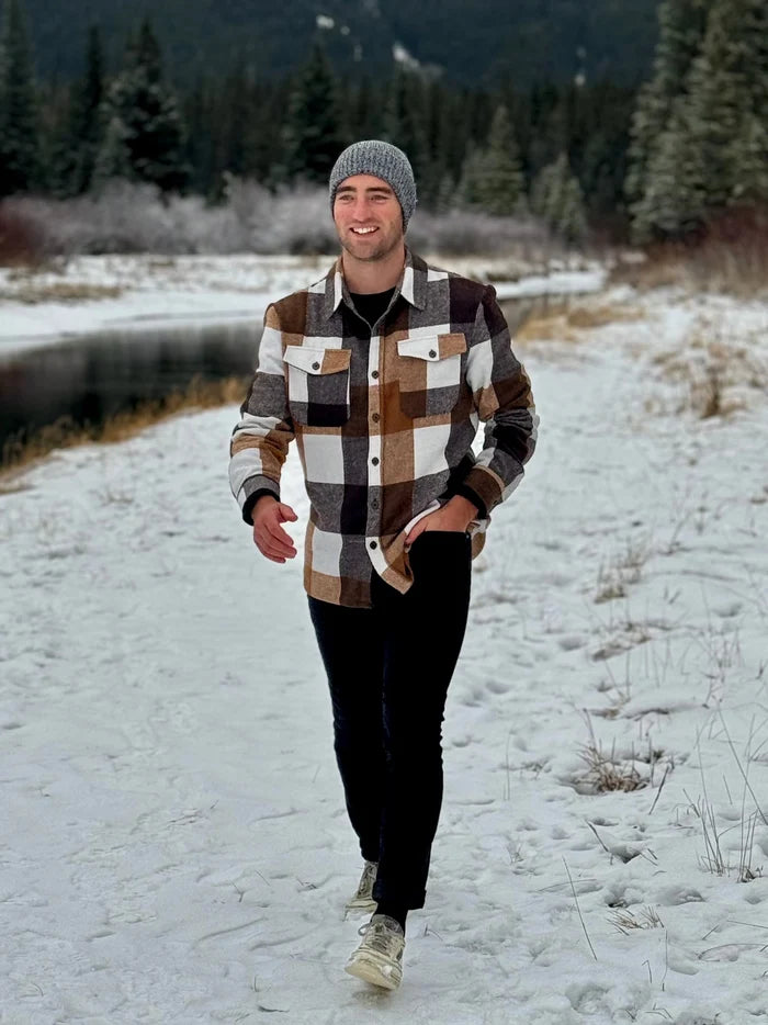 Man walking in the snow wearing our cozy flannel shacket in camel squares in Banff, Canada.