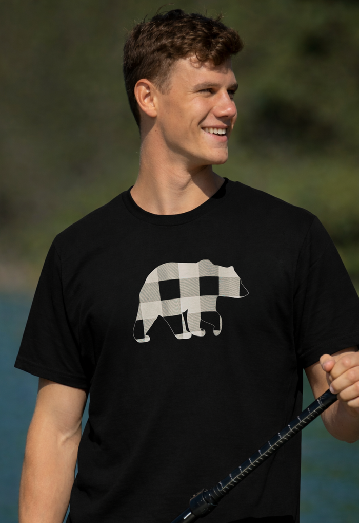 Man wearing a black t-shirt with a bear graphic, holding a fishing rod outdoors.