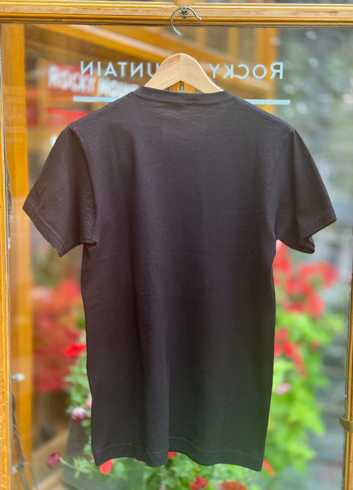 Black t-shirt on a hanger with a blurred background of flowers and a store entrance.