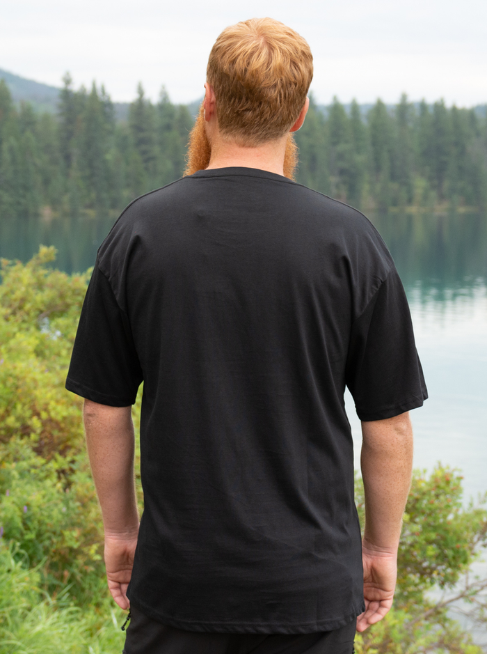 Man wearing a black t-shirt with a scenic background of trees and water