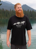 Man wearing a black t-shirt with 'Banff Canada' design standing by a lake with mountains in the background.