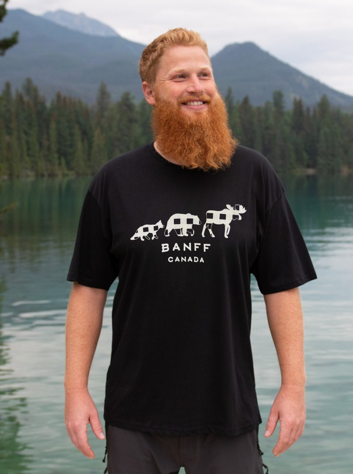 Man wearing a black t-shirt with 'Banff Canada' design standing by a lake with mountains in the background.