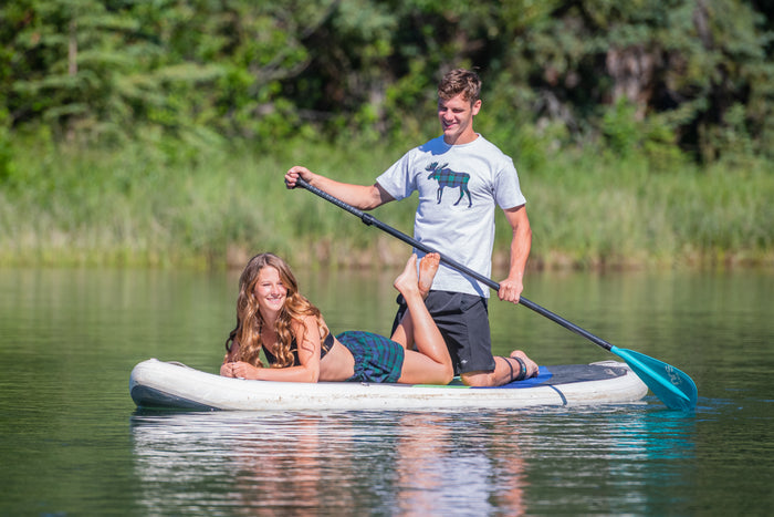 Two people on a paddleboard in a lake with trees in the background