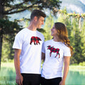 Two people wearing white t-shirts with red and black buffalo check animal designs in a natural setting.