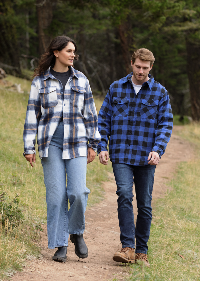 A man wearing a royal blue and black buffalo check padded flannel camping outdoor jacket with jeans.