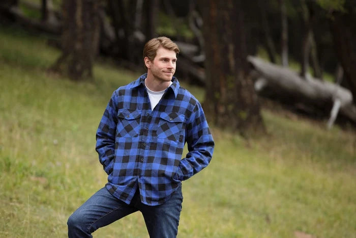 A man wearing a royal blue and black buffalo check padded flannel camping outdoor jacket with jeans.